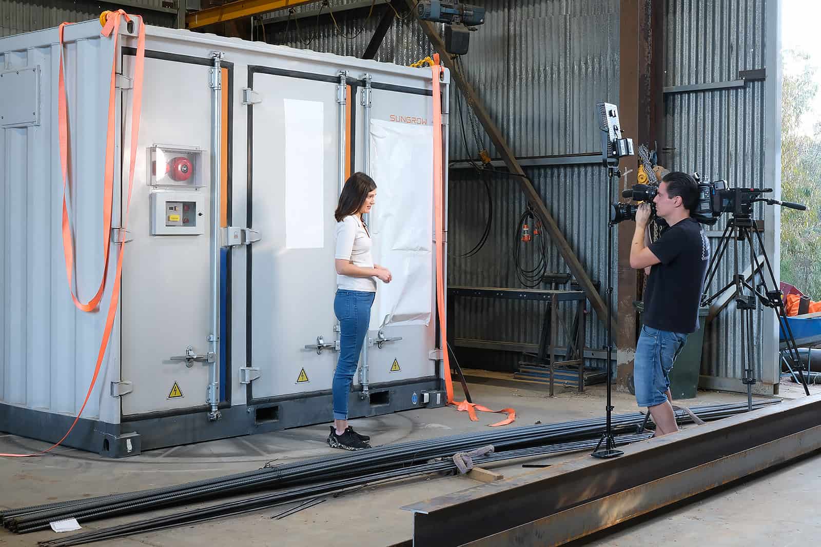A woman is being filmed in front of what looks like a small shipping container