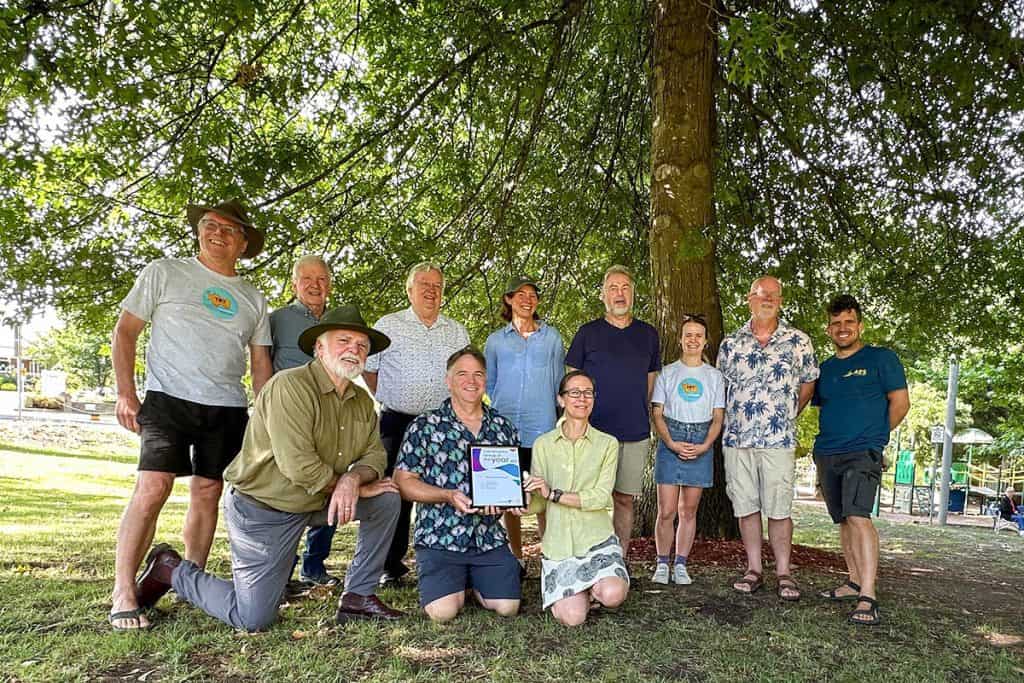 Ten TRY committee members and Indigo Shire councillor Peter Croucher stand under a tree showing the framed certificate commemorating the award.