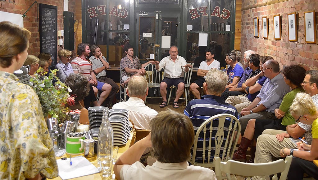 A group of people sit in a circle in a cafe listening to someone speak
